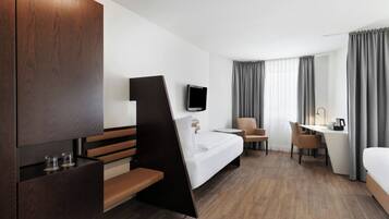 Een moderne hotelkamer met een bed, bureau, stoel en een aan de muur bevestigde televisie.
