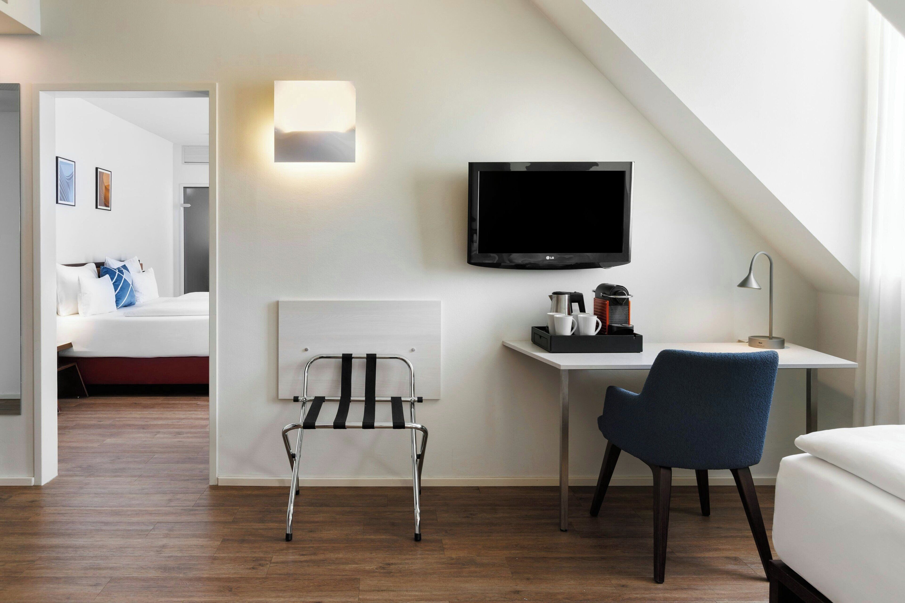 Une chambre d’hôtel moderne avec un plafond en pente, un lit, un bureau avec une chaise, un téléviseur et un fauteuil roulant.