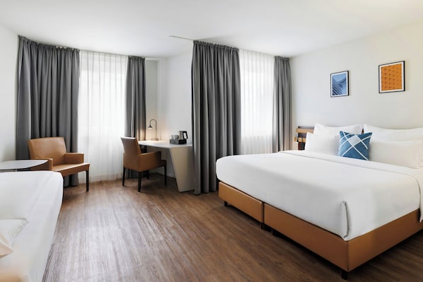 Una habitación de hotel con una cama grande, un escritorio con una silla, una mesita pequeña y un sofá.
