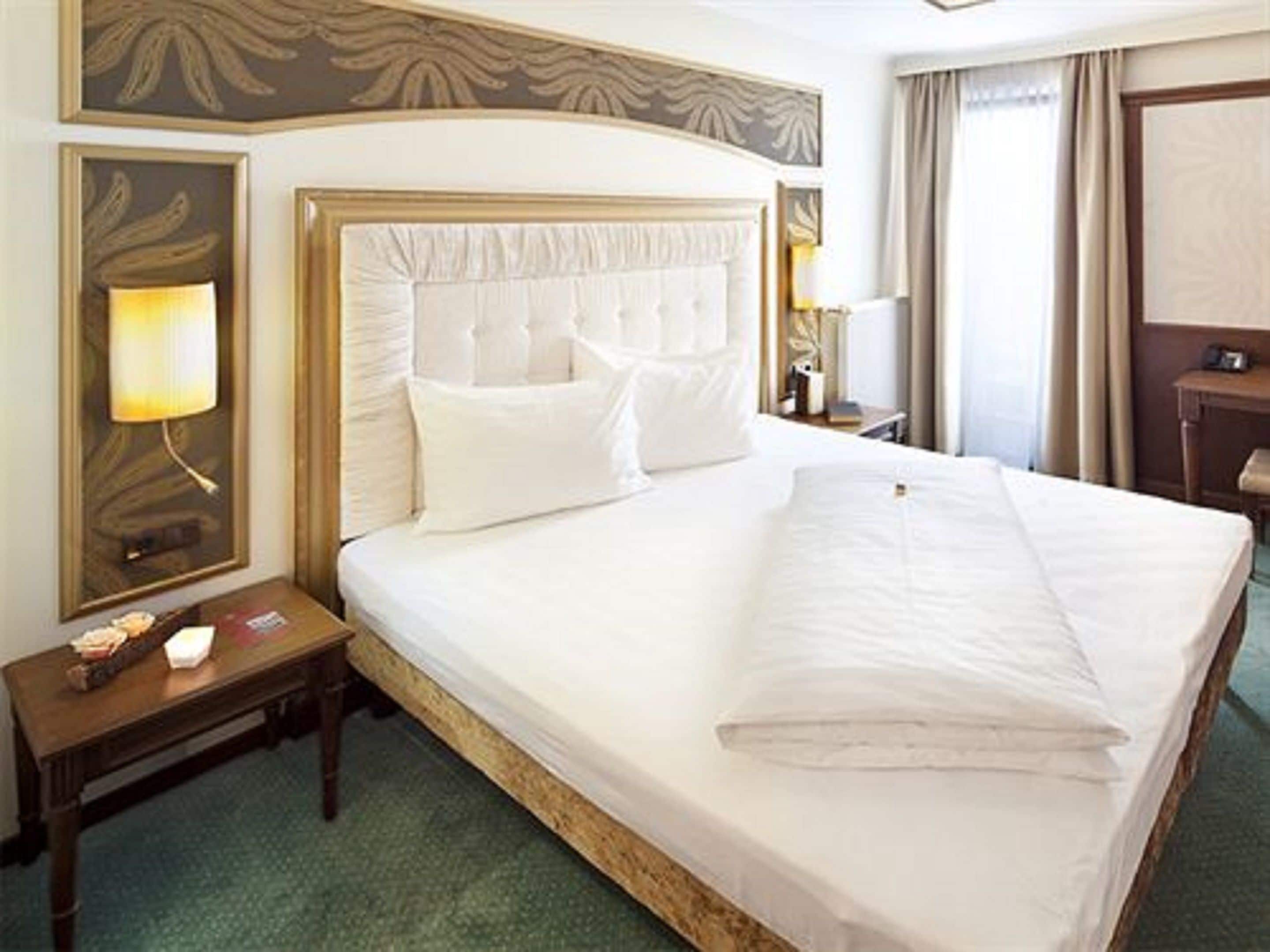 Quarto de hotel com uma cama grande, mesa de cabeceira, abajur e espelho.