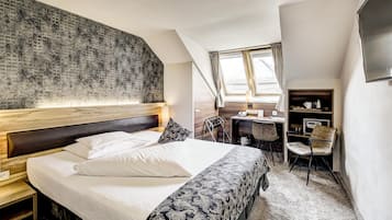 A hotel room with a bed, a desk, a chair, a TV, and a window with curtains.