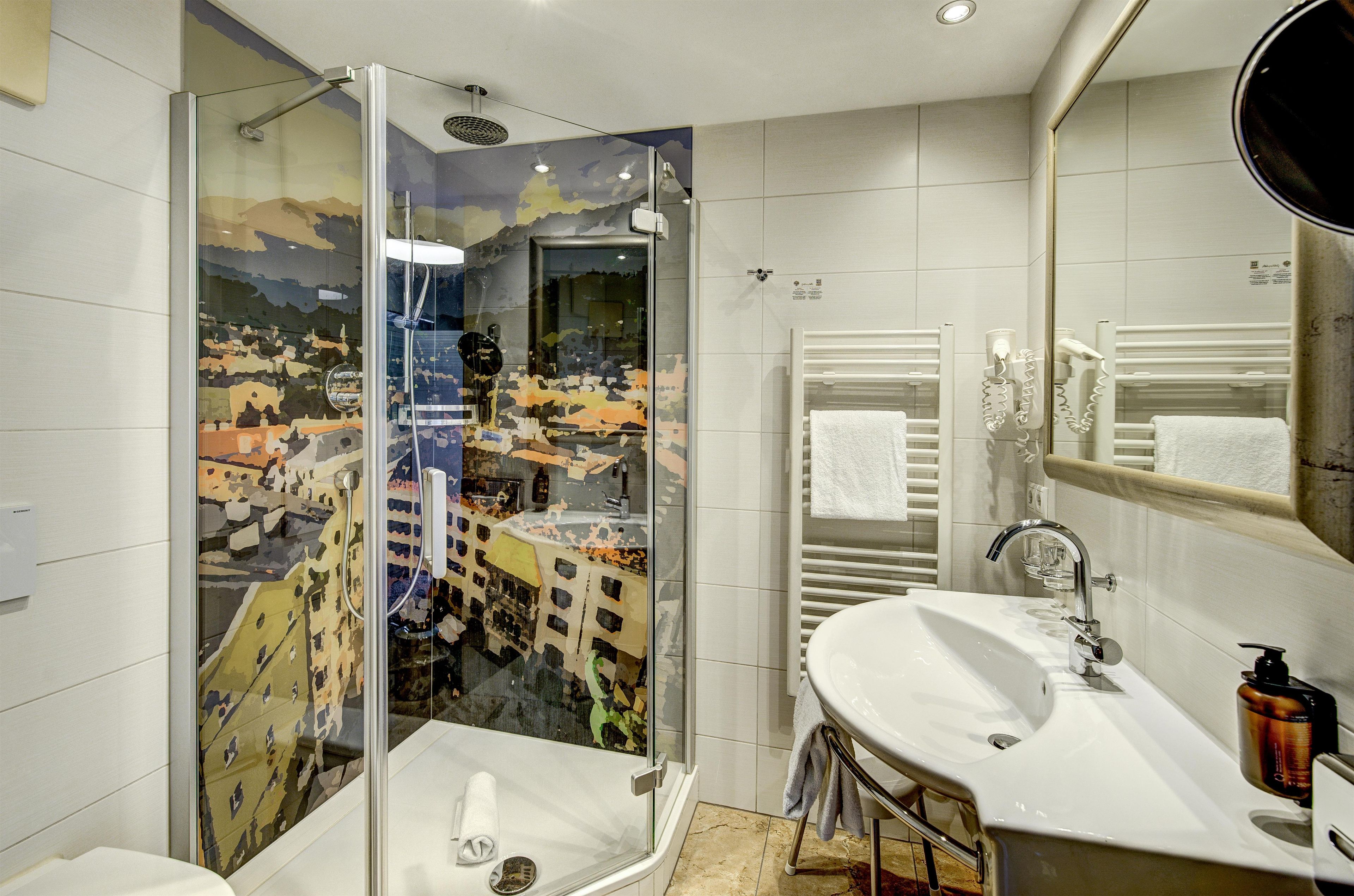 A modern bathroom with a glass-enclosed shower, a white sink, and a mirror with a towel rack.