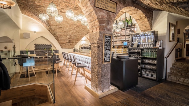 A bar area with exposed brick walls, wooden bar counters, and hanging crystal light fixtures.