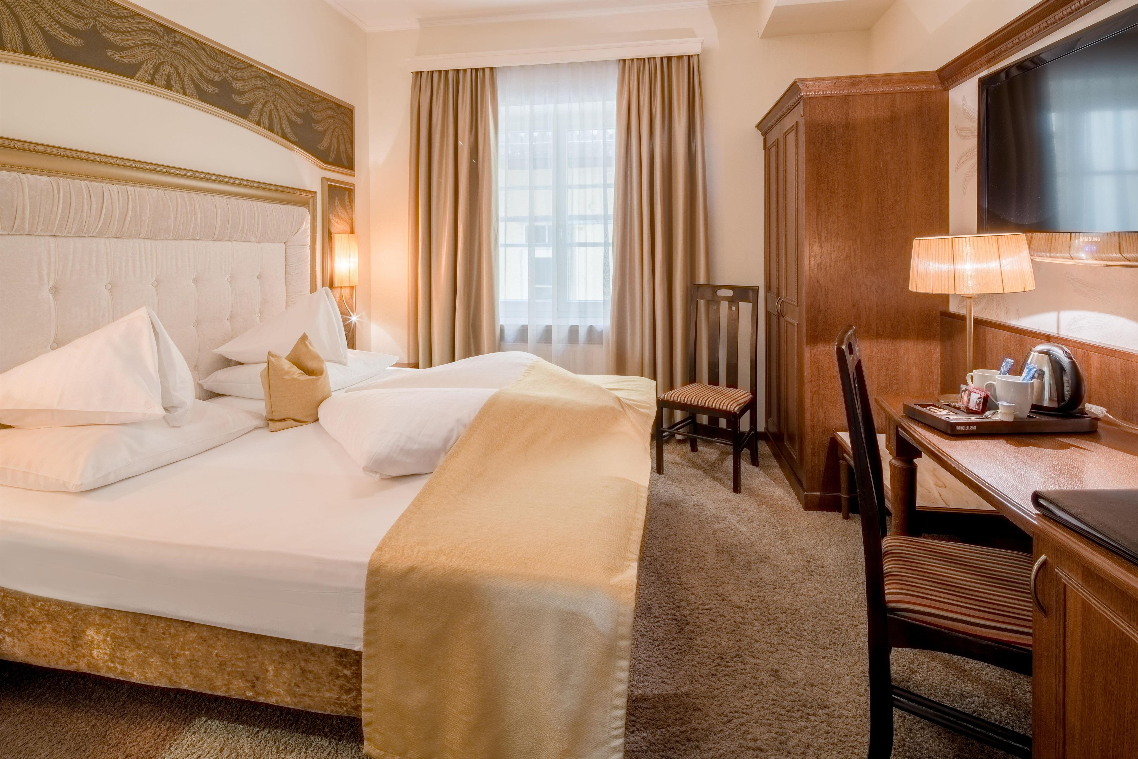 A hotel room with a large bed, a desk with a chair, a television, and a window with curtains.