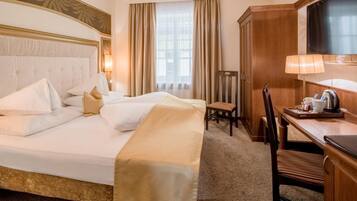 A hotel room with a large bed, a desk with a chair, a television, and a window with curtains.