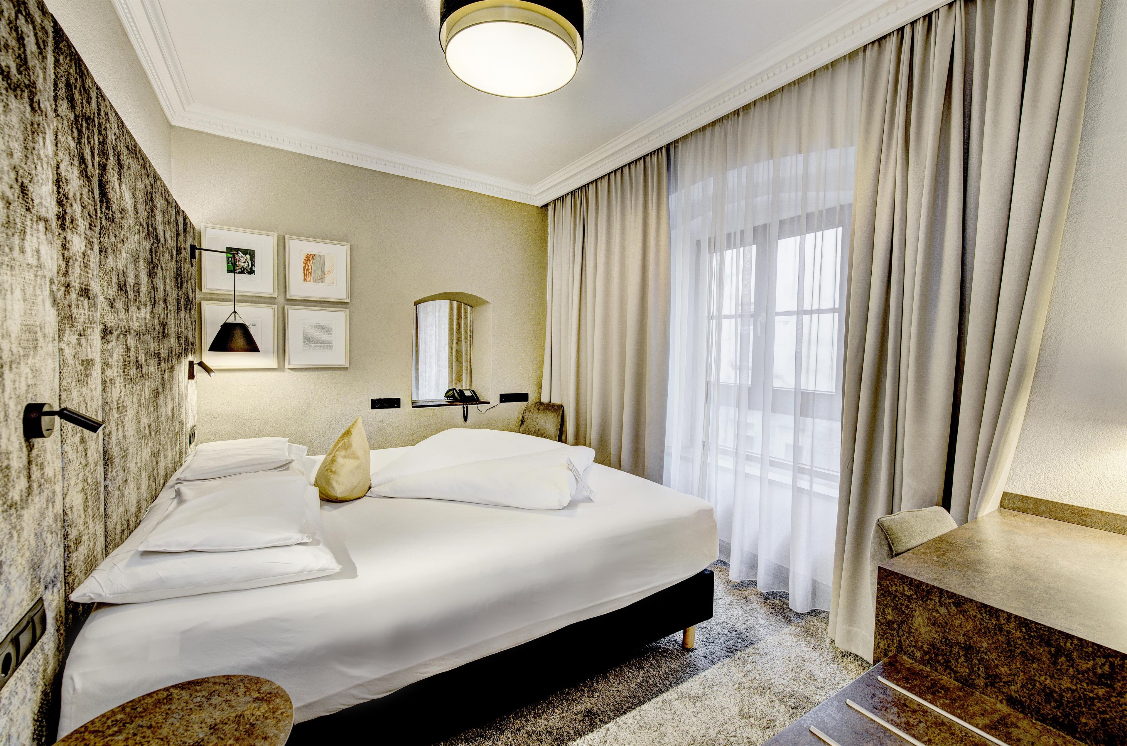 Ein Hotelzimmer mit einem großen Bett, einem Schreibtisch, einem Stuhl, einem Spiegel und einem Fenster mit Vorhängen.