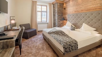 Habitación de hotel con una cama grande, un escritorio con teléfono, una silla, una ventana con cortinas y una pared decorativa de piedra.