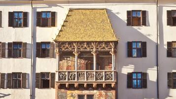 Un edificio histórico con un balcón central, múltiples ventanas y un patio con gente y mobiliario exterior.