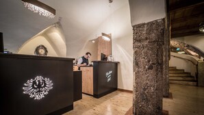 Un espace d’accueil avec un bureau en bois, un pilier en pierre et une horloge au mur.