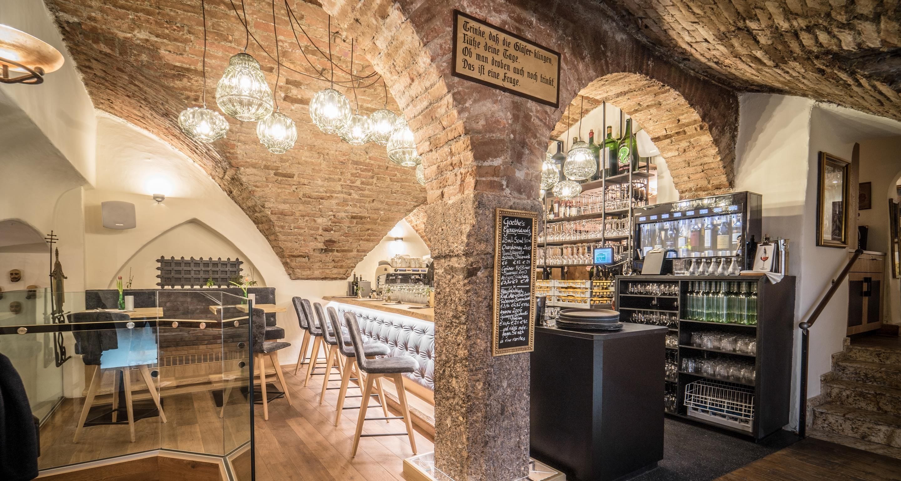 Zona de bar con techo de ladrillo, lámparas colgantes y una pizarra de menú.