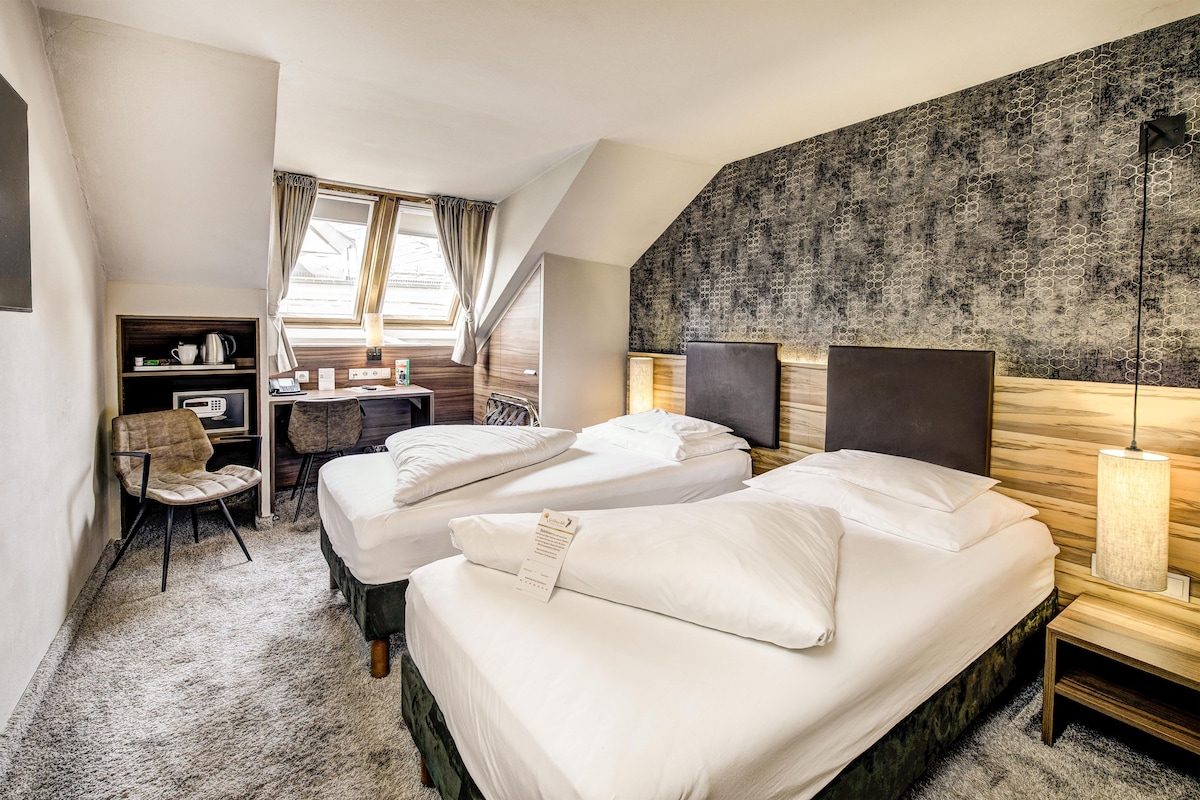 Une chambre d’hôtel avec deux lits, un bureau, une chaise et une grande fenêtre.