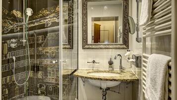 Un baño con cabina de ducha de vidrio, un lavamanos con encimera de mármol y un espejo grande con marco decorativo.
