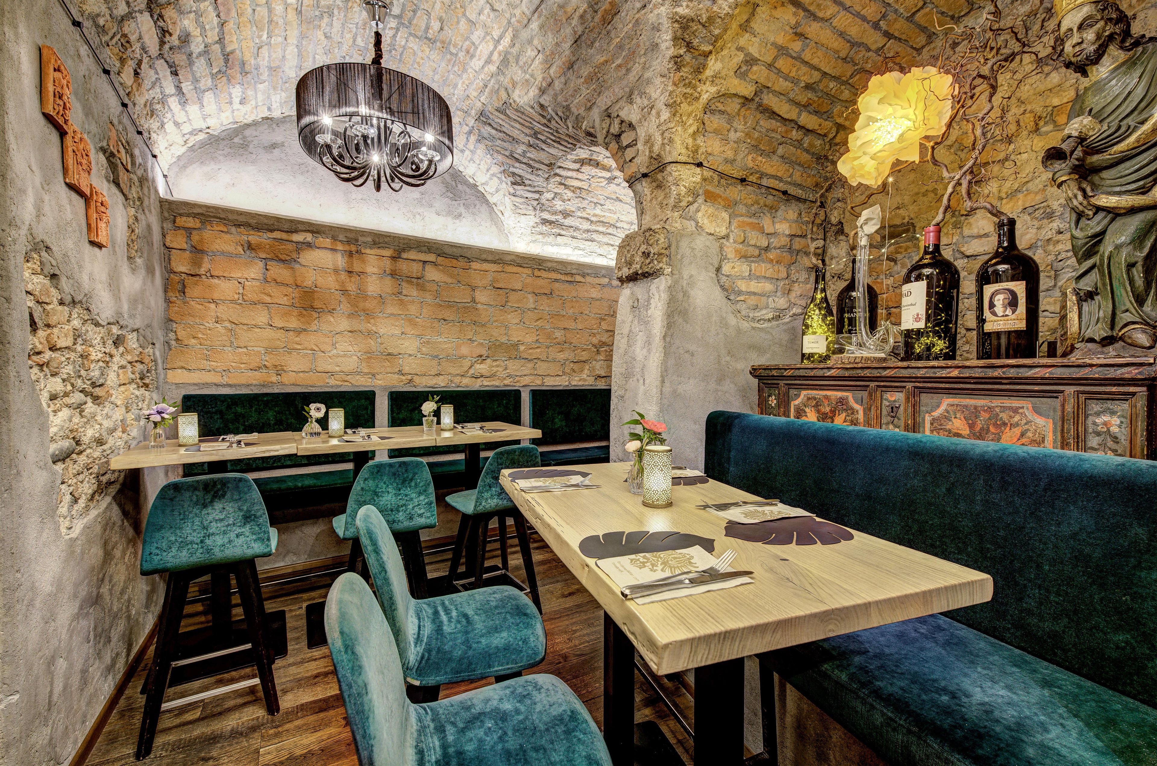L’intérieur d’un restaurant avec des murs en briques, un lustre, des tables en bois et des sièges recouverts d’un tissu bleu.