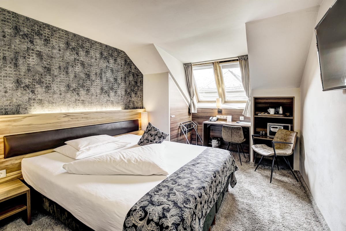A hotel room with a large bed, a desk with a chair, a TV, and a window with curtains.