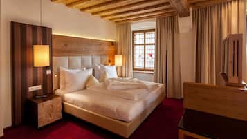 Habitación de hotel con una cama grande, cabecera de madera, mesita de noche, cómoda y ventana con cortinas.