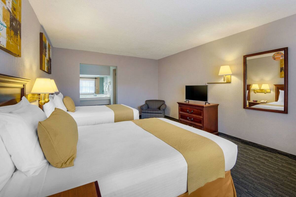 A hotel room with two beds, a TV, a desk, a chair, and a bathroom mirror.