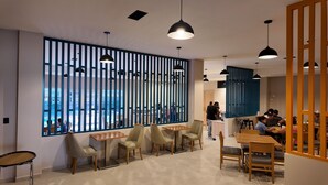 A modern interior with high tables and chairs, pendant lighting, and a view through a blue partition.