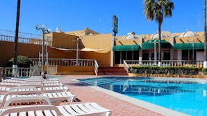 A swimming pool area with white lounge chairs, a brick pathway, and a building with a green awning and a sign.