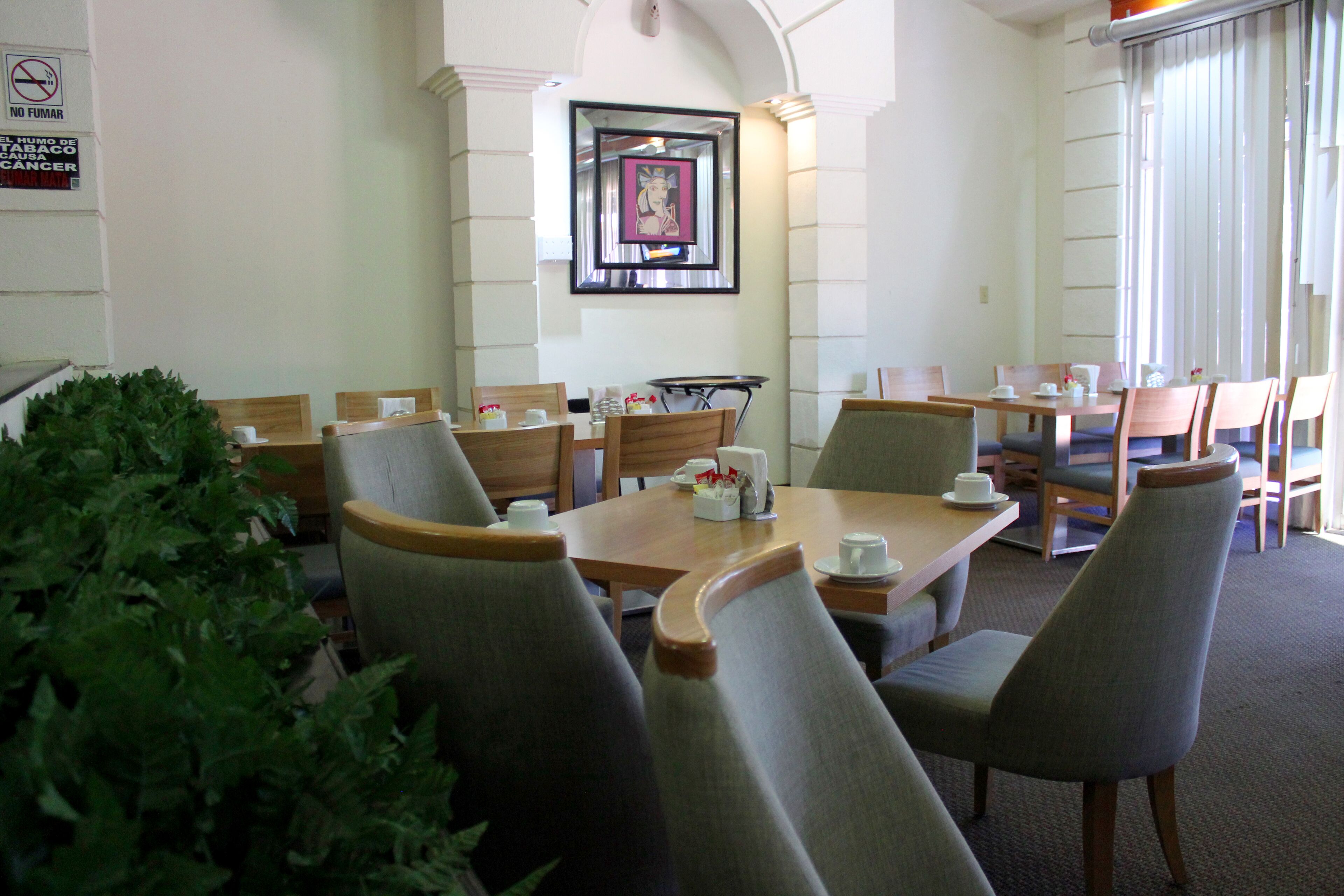 A conference room with tables and chairs, a framed picture on the wall, and a no-smoking sign.