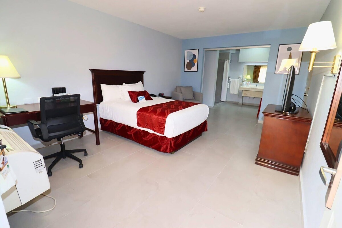 A hotel room with a bed, desk, chair, and a bathroom visible through an open door.