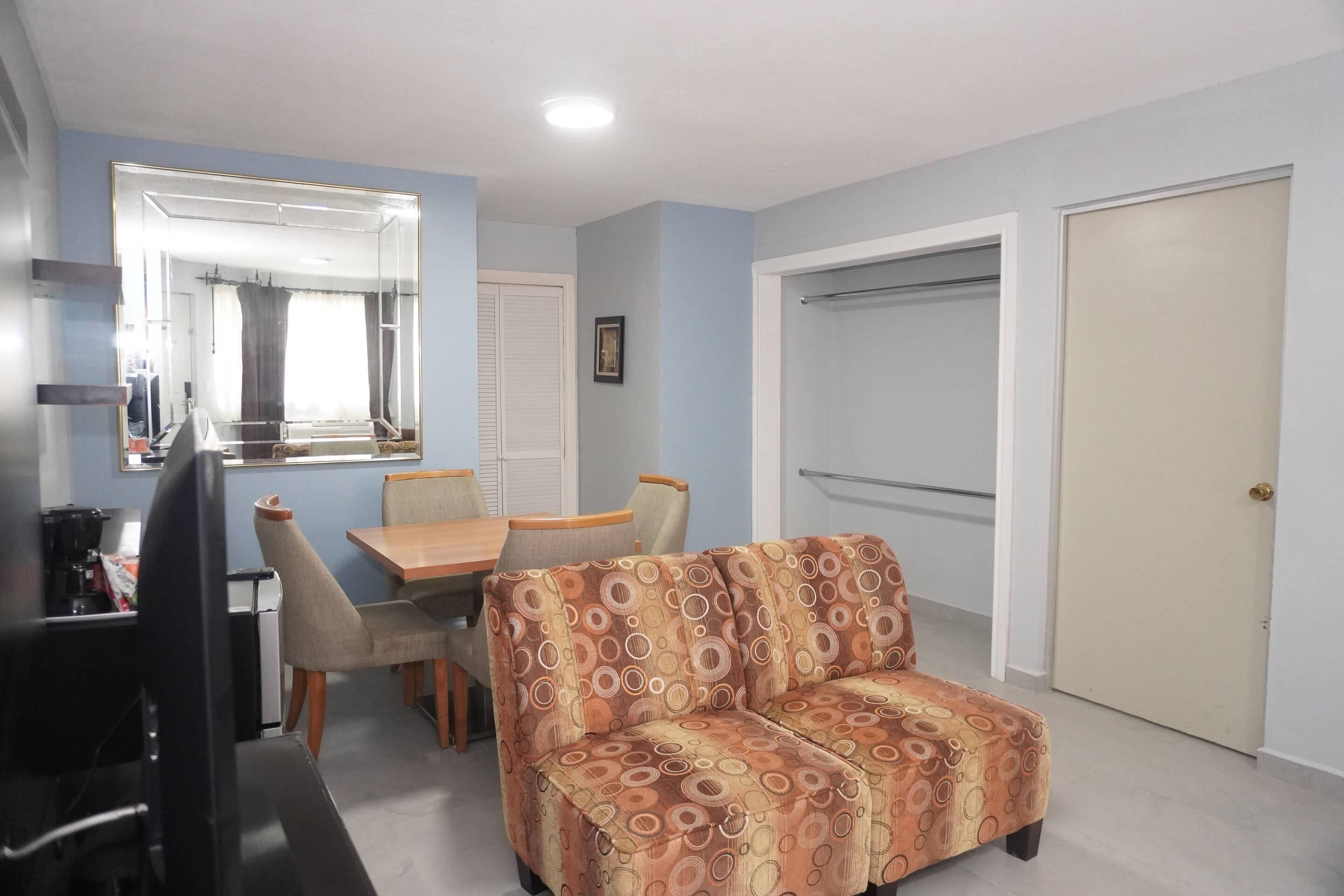 Une pièce comprenant un canapé, une table à manger avec des chaises, un téléviseur, un miroir et une porte.