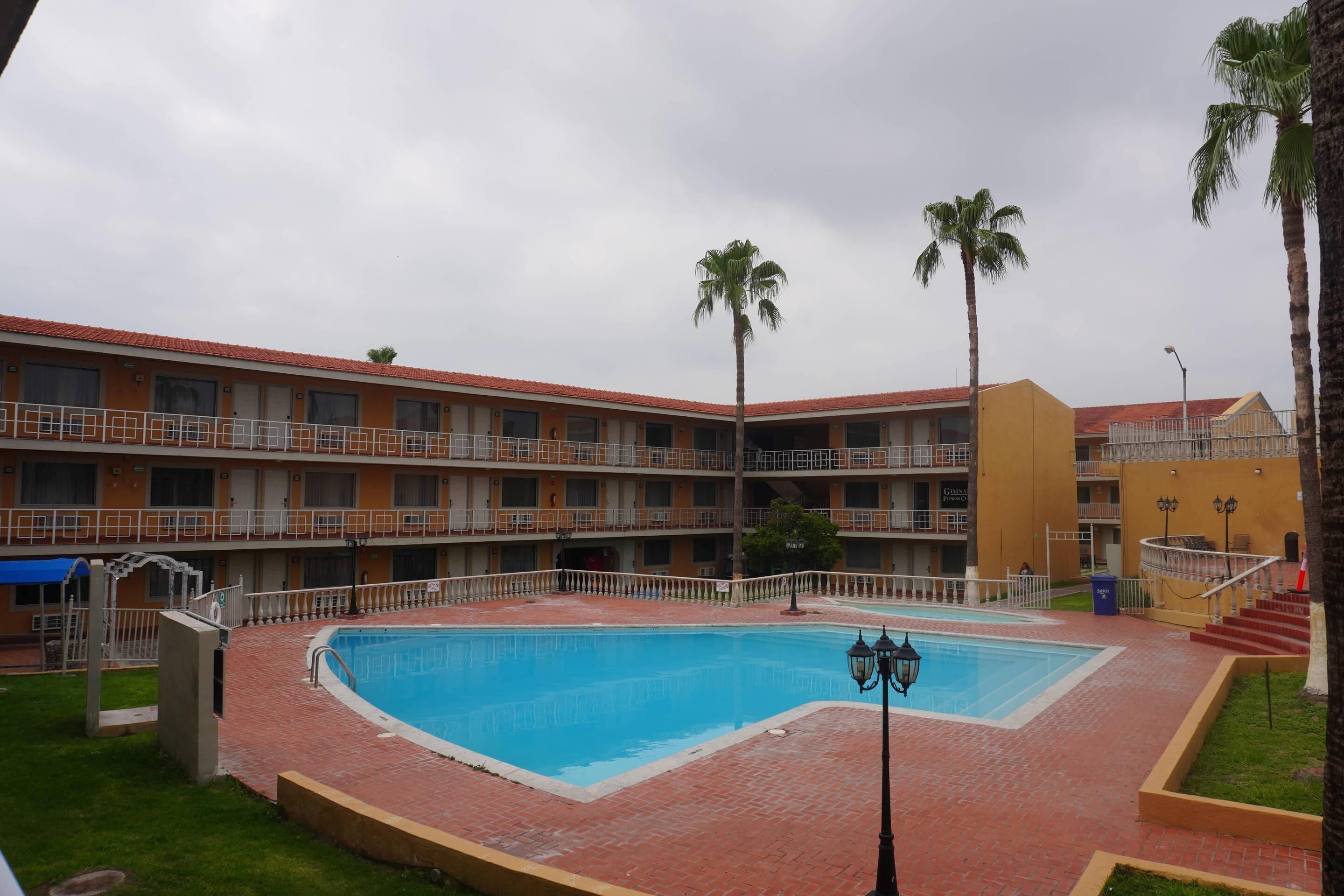 A hotel with a swimming pool, multiple balconies, and palm trees.