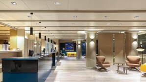 Un moderno vestíbulo de hotel con mostrador de recepción, zona de estar y una gran pantalla que muestra una vista panorámica.