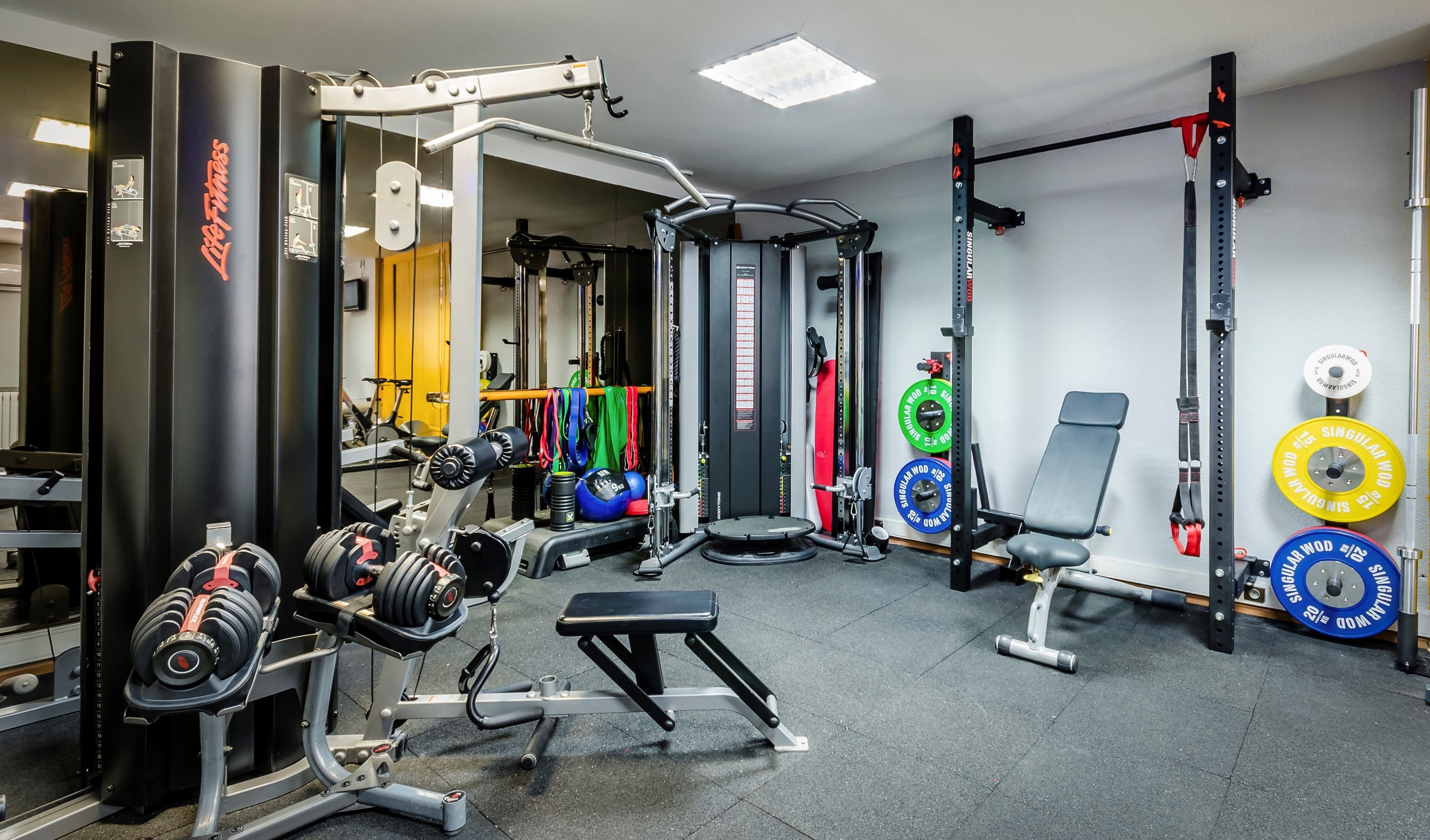 Une salle de sport équipée de matériel de musculation, de bancs et d’un support pour les exercices de squat.