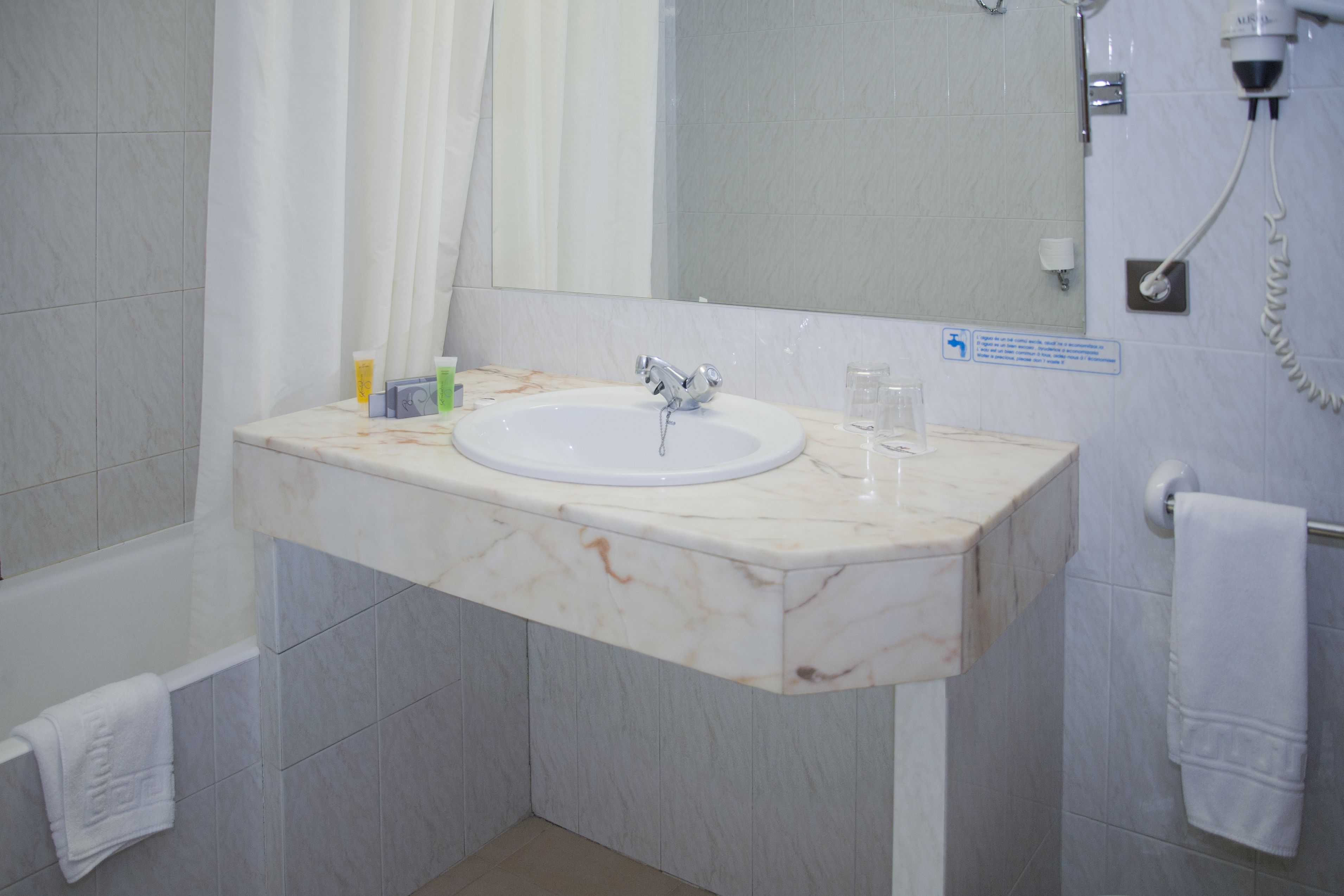 A bathroom with a marble sink, a mirror, a shower, and a towel rack.