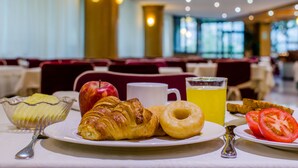 Un desayuno con cruasanes, un donut, un vaso de jugo de naranja, un plato de rebanadas de manzana y una taza, además de un plato con rodajas de tomate.
