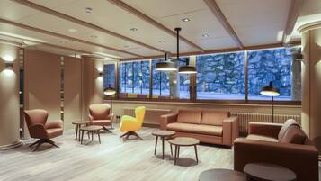 A modern lobby with leather sofas, round tables, and large windows with a view of a snowy landscape.