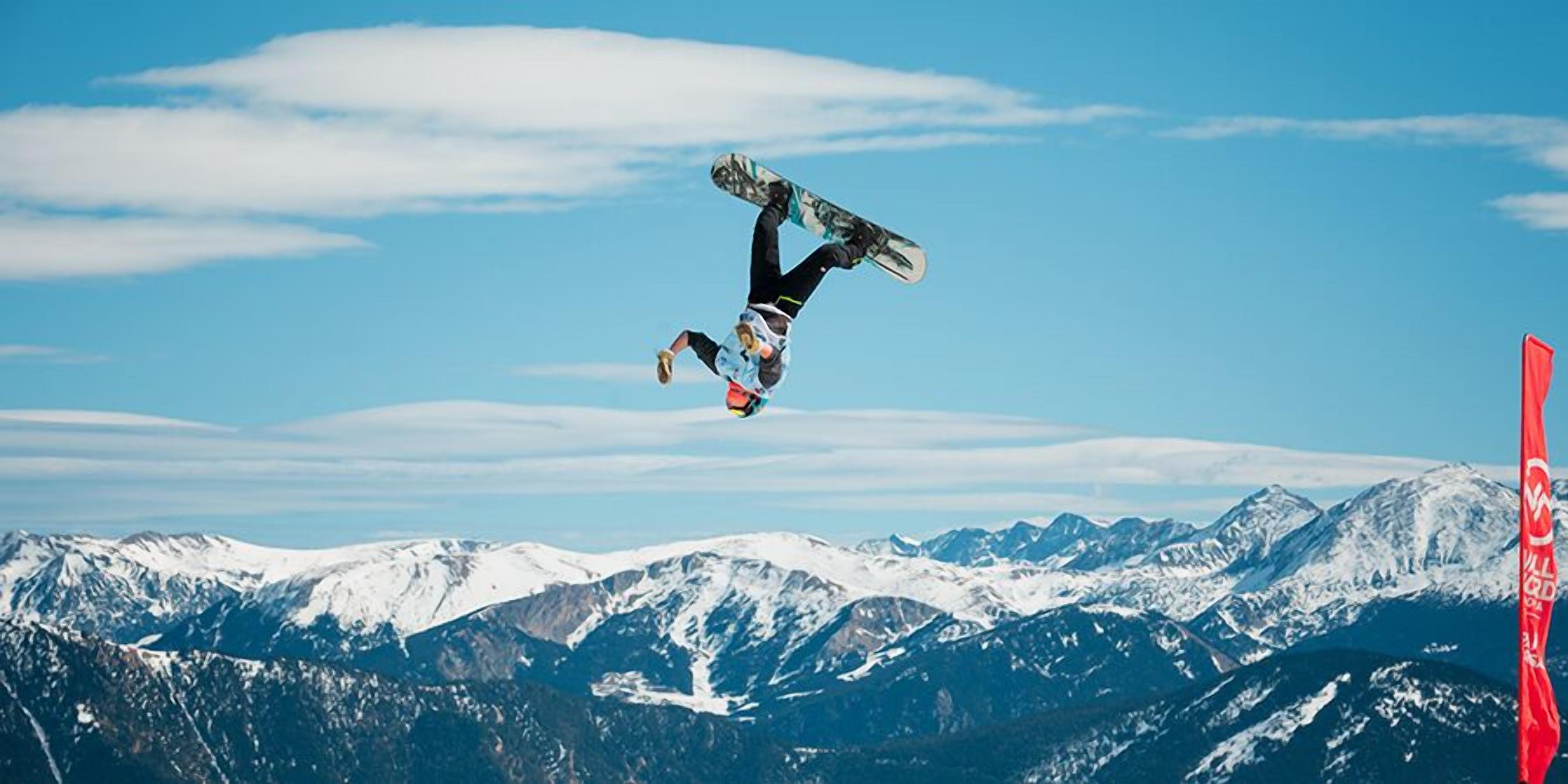 A snowboarder performing a trick against a backdrop of snow-covered mountains.