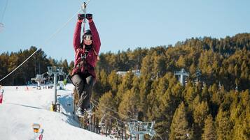 En person suser ned på en zipline over et snelandskab med træer i baggrunden.