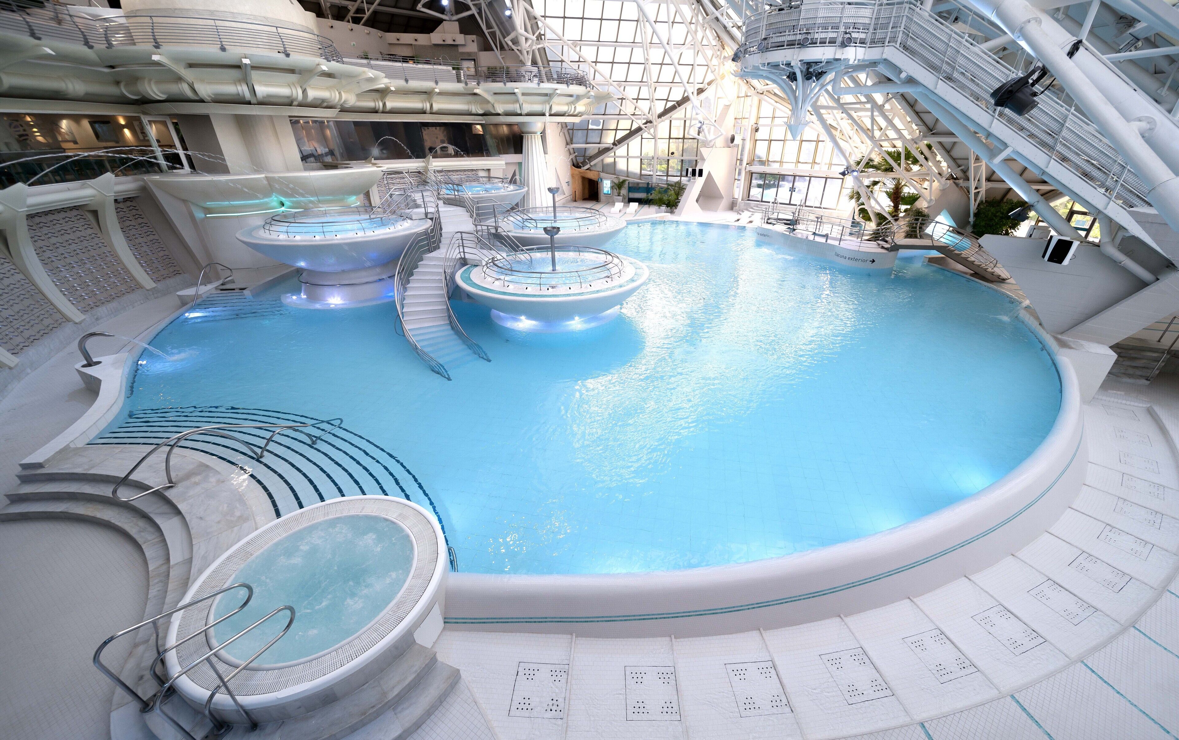 A large indoor swimming pool with multiple water features, including a central fountain and surrounding water jets.