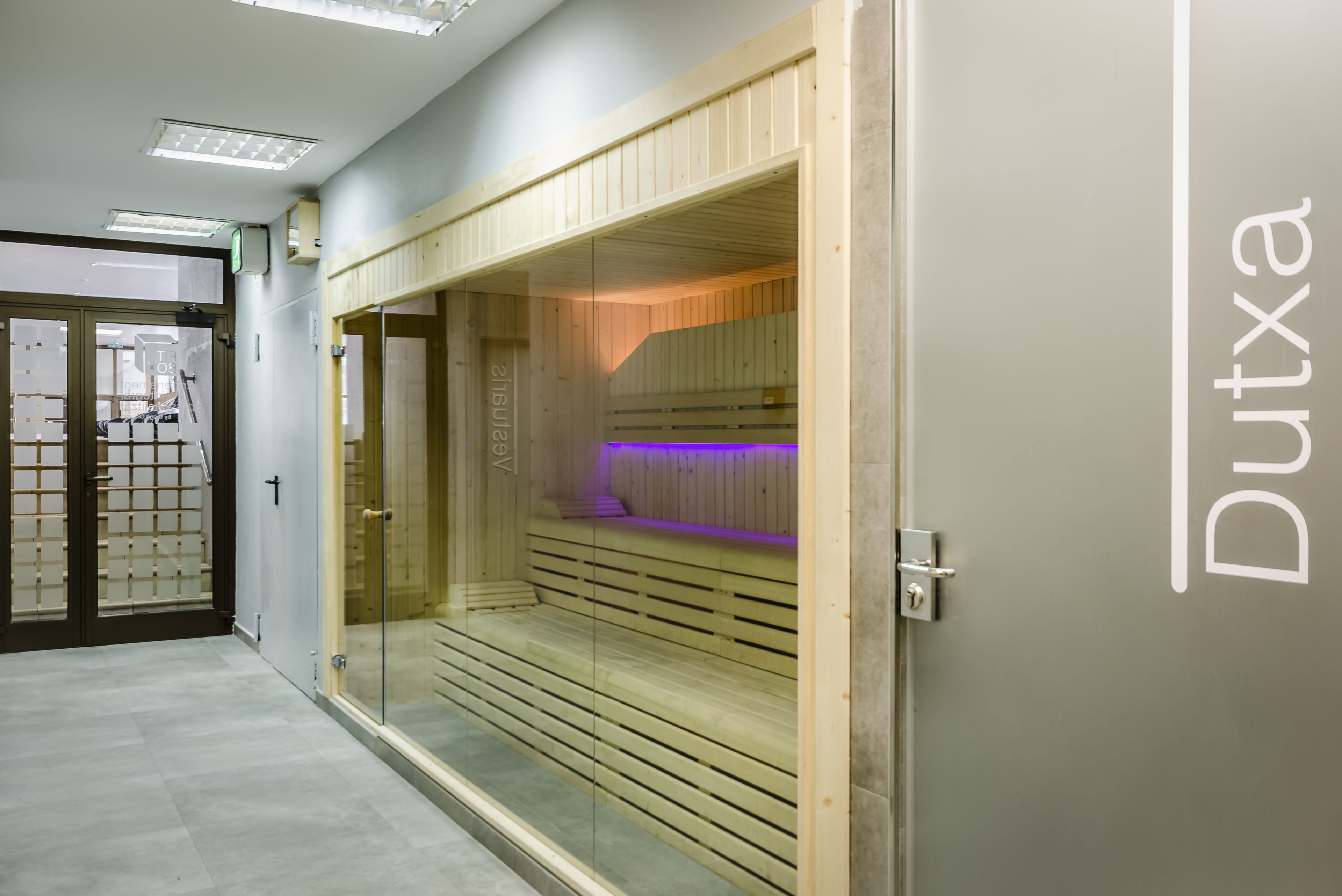 Un interior moderno con una zona de sauna de madera, puertas de cristal y un cartel que dice "Dutxa".