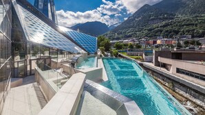 Un hotel moderno con piscina, fachada de vidrio y montañas al fondo.