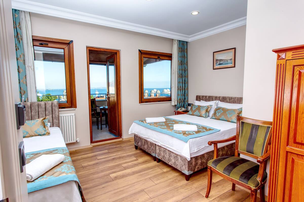 A hotel room with a large bed, a wooden chair, a desk, and a view of the sea.