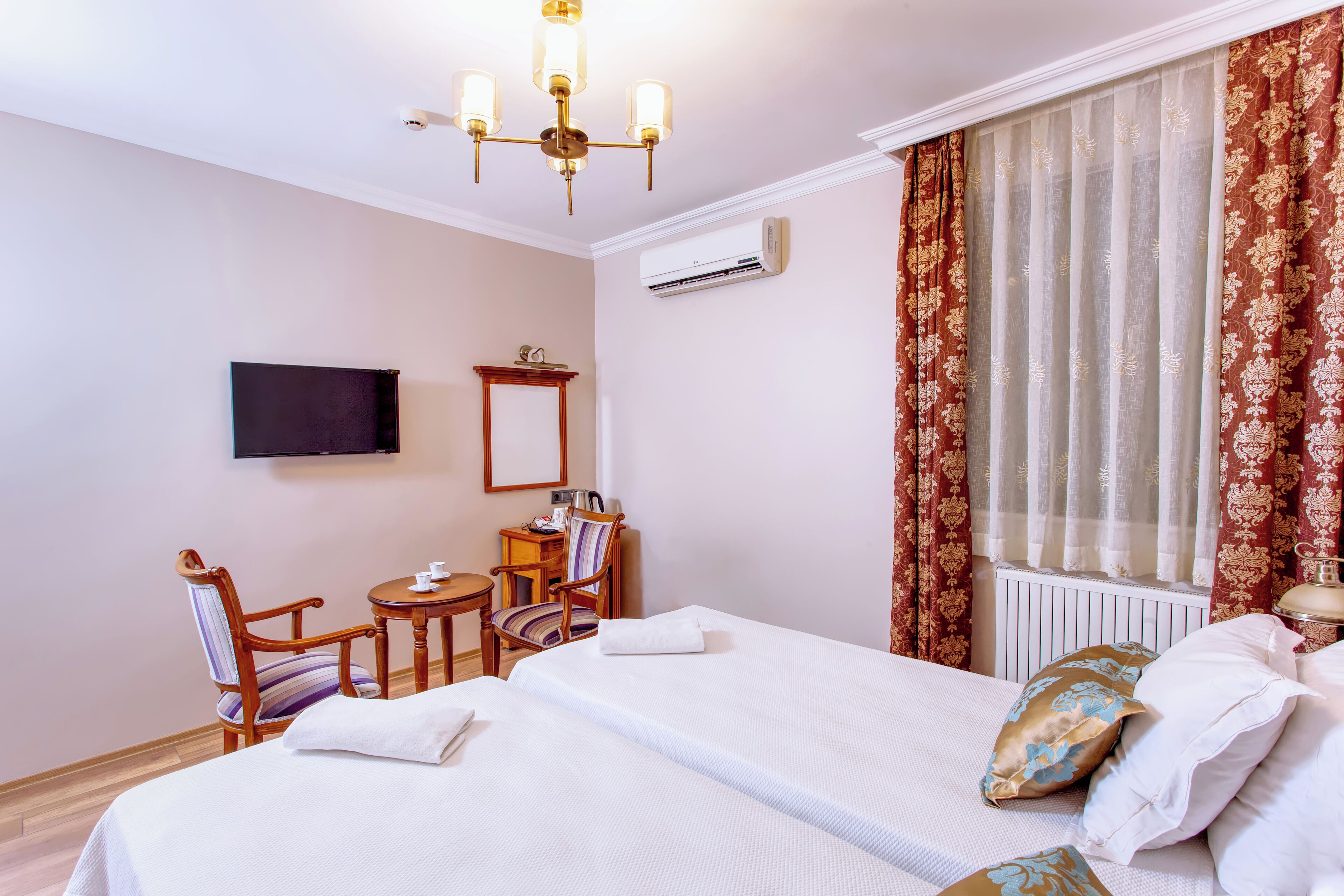 A hotel room with two beds, a TV, a desk with a chair, and a window with curtains.