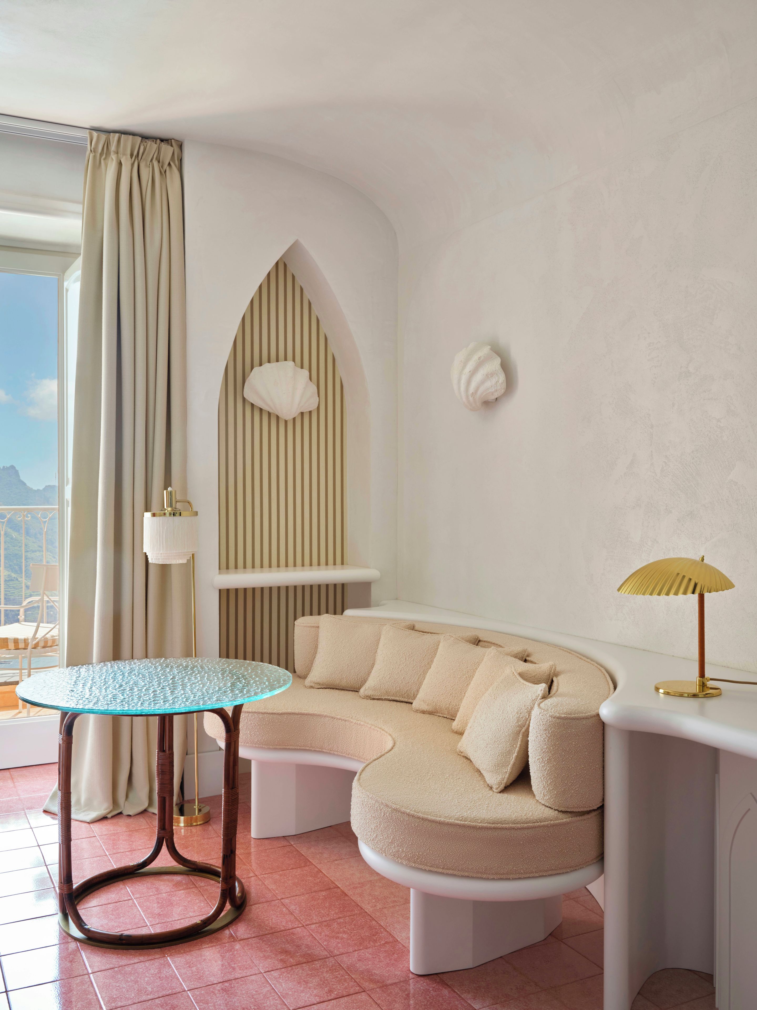 Una sala de estar moderna con una mesa de vidrio, un sofá curvo, una lámpara y vistas a las montañas.
