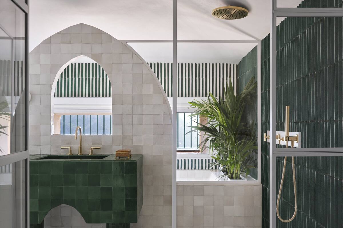 Un baño moderno con un lavamanos con azulejos verdes, un ventanal arqueado blanco y una ducha con pared verde.