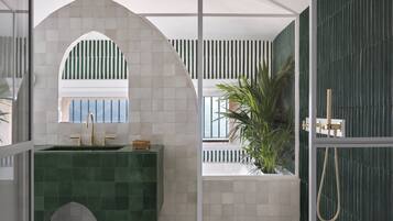 Uma casa de banho moderna com uma pia em azulejo verde, uma janela em arco branca e um chuveiro com parede verde.