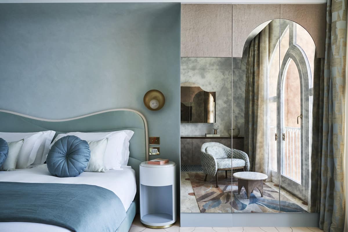 Un dormitorio con cama, mesita de noche y vistas a un balcón con una silla y una mesa.