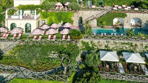 A large hotel with multiple balconies, a swimming pool, and lush gardens.