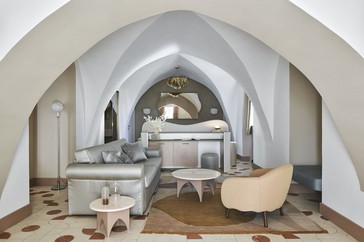 Un interior moderno con sofá, sillón y zona de comedor bajo un techo abovedado.