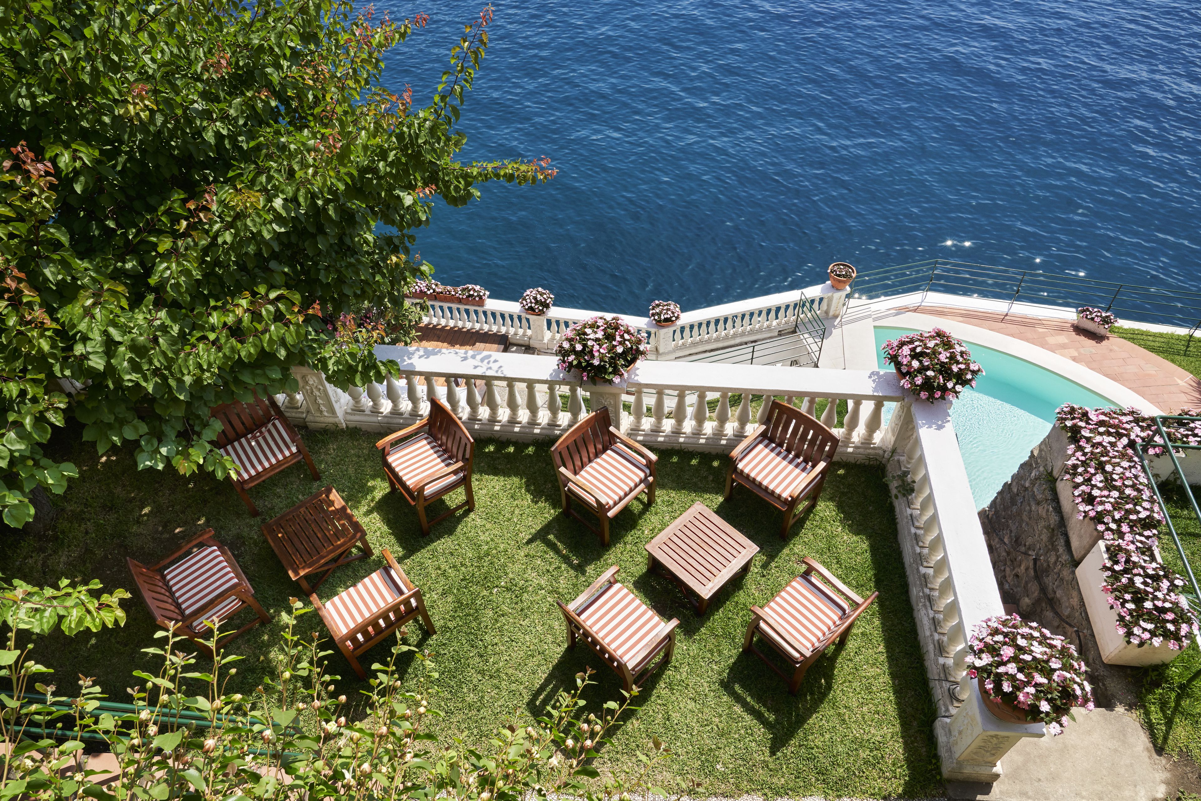 A poolside area with wooden lounge chairs and a white balustrade overlooking the sea.