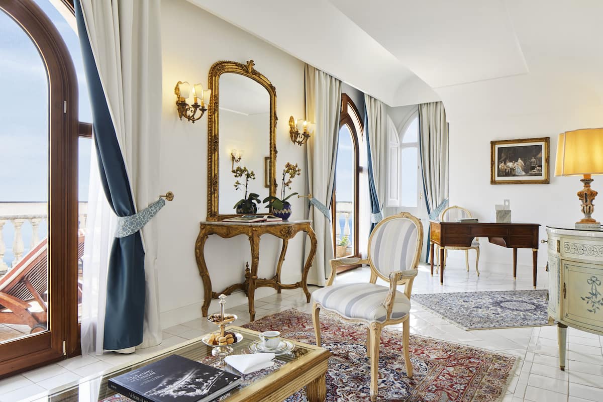 Una habitación con un espejo grande, un escritorio de madera, una silla, una mesa de comedor y una bandeja de pasteles sobre un tapete estampado.