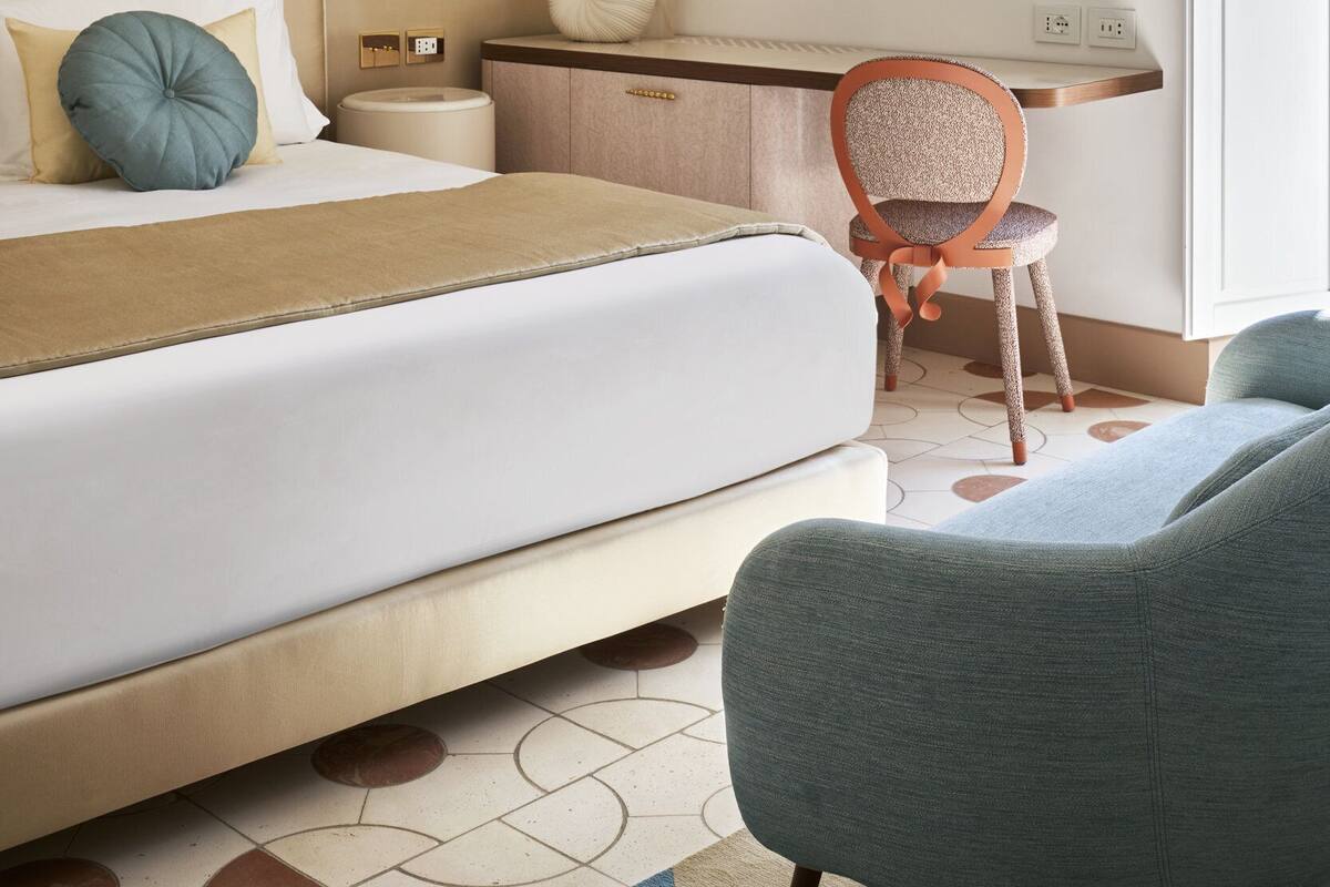 Habitación de hotel moderna con cama, escritorio y una silla. Se observan apliques de pared y un jarrón con flores.