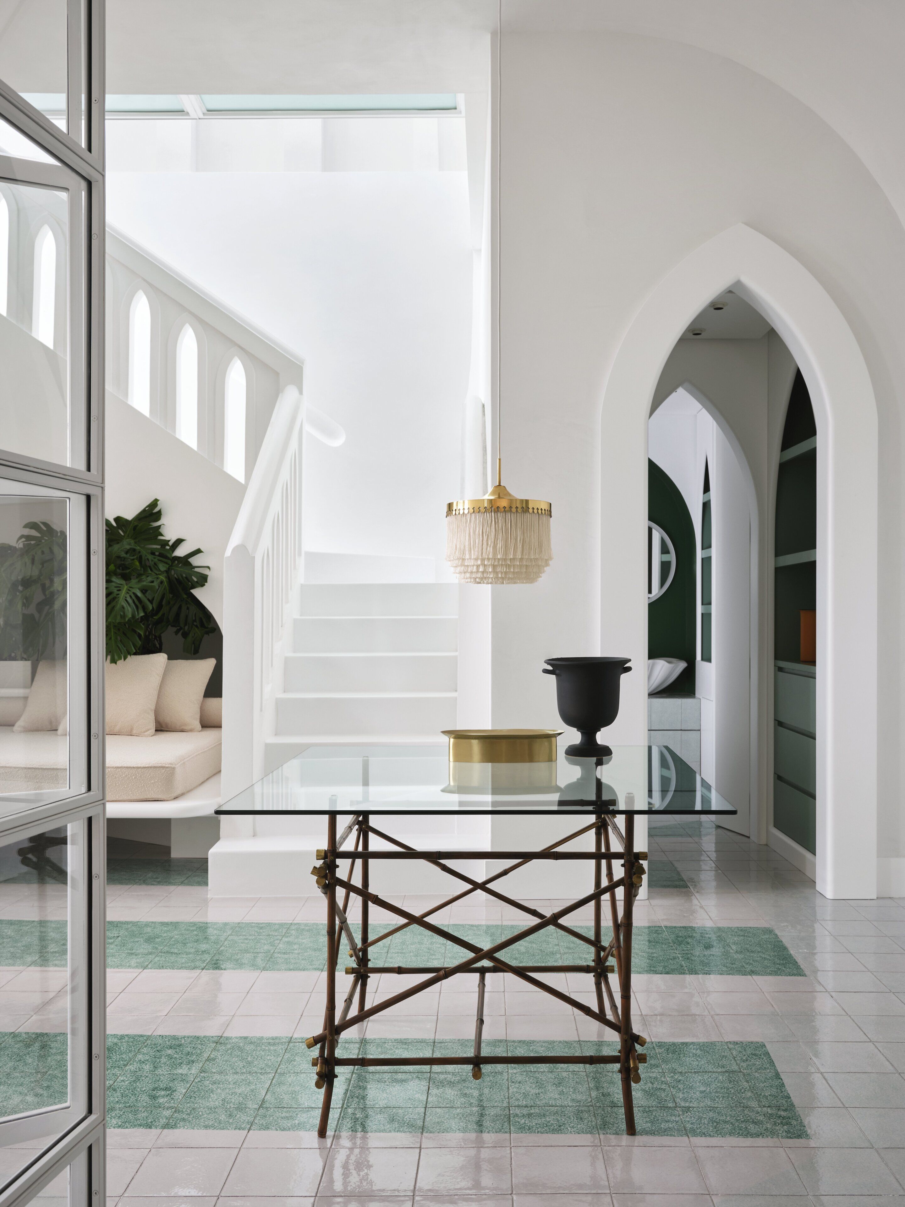 Un intérieur moderne avec une table en verre, un luminaire suspendu et un escalier doté de rampes blanches.