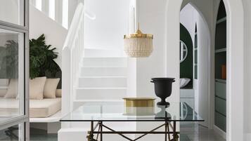 Un intérieur moderne avec une table en verre, un luminaire suspendu et un escalier doté de rampes blanches.