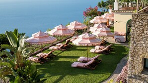 A pool area with lounge chairs and umbrellas, a stone building, and a view of the ocean.